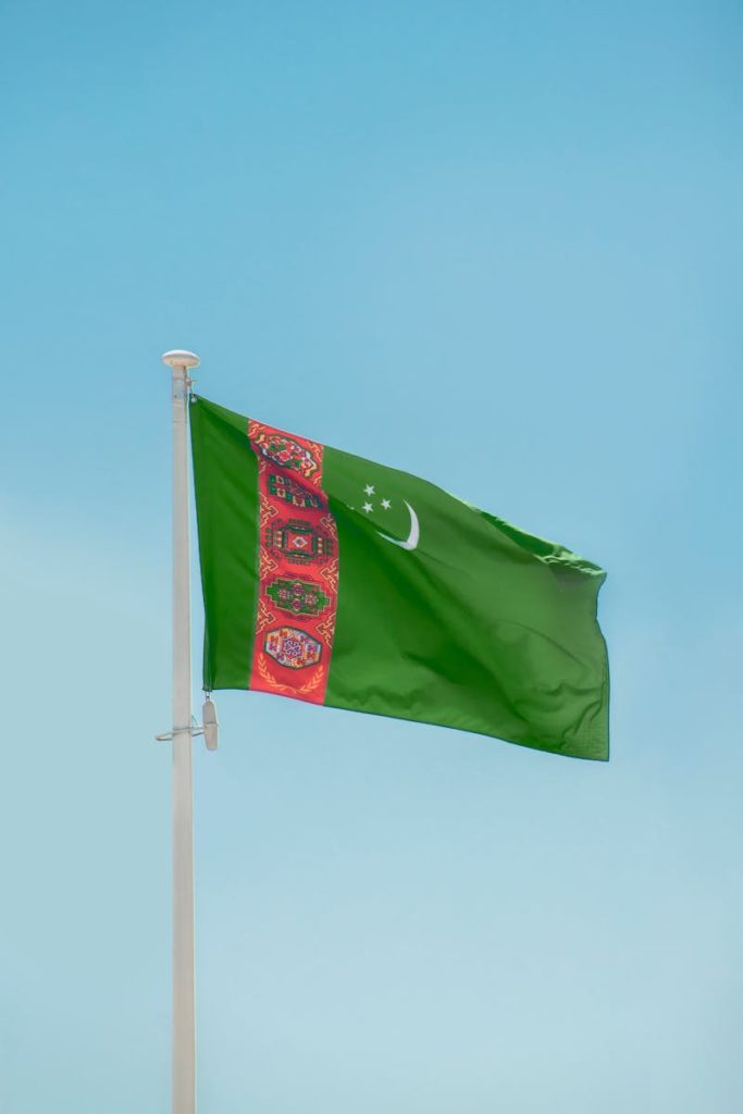Turkmenistan flag waving on a flagpole with a clear blue sky in the background, symbolizing national pride.